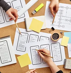Hands sketching app wireframes and a flowchart on paper beside sticky notes